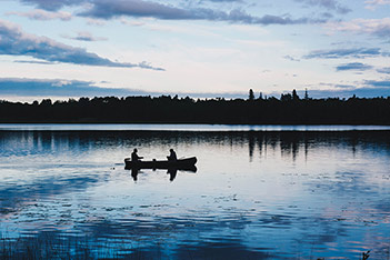 Photo shows two people in a boat on a midnight lake.