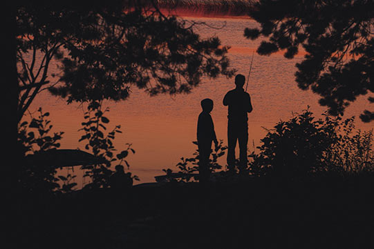 Photo shows two small boys having their favourite summer activities, angling fish in a dusk.