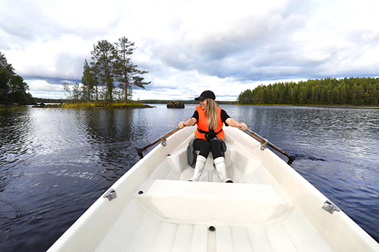 Villa-Cone-Beach-Row-Boat Photo shows a young woman rowing a white boat across the protected Lake Kuivajarvi. No one is at sight.